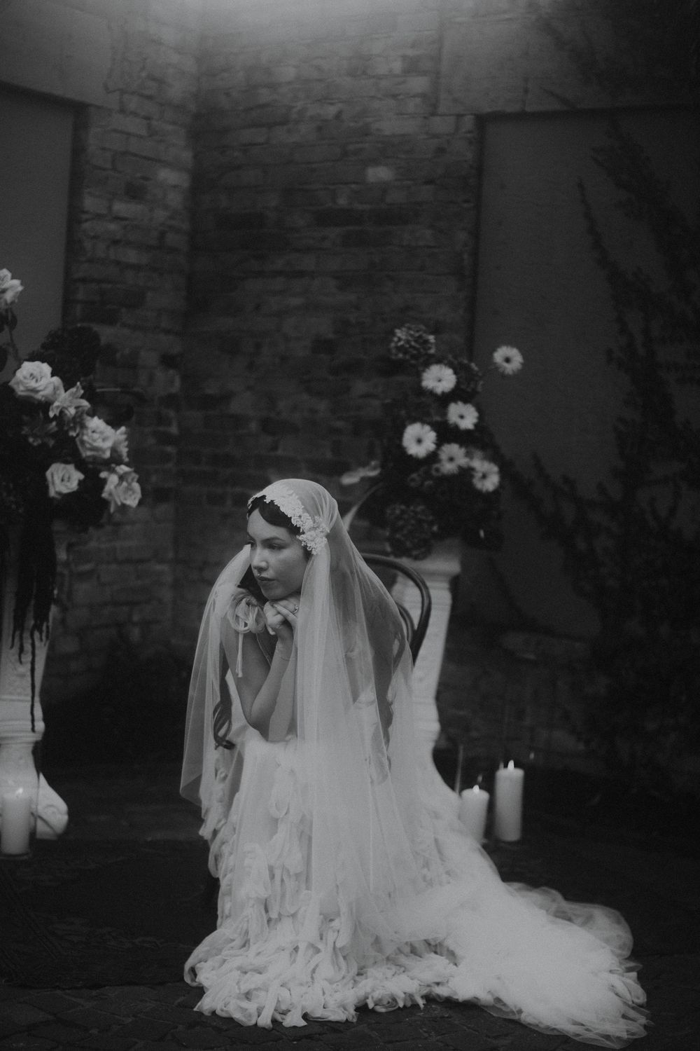 Ethereal bridal portrait with flowing white veil against brick wall backdrop.