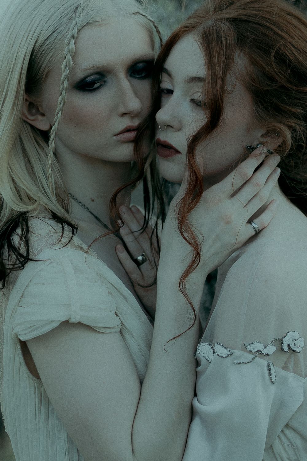 Two models in ethereal white outfits pose intimately together in a desaturated artistic fashion photoshoot series.