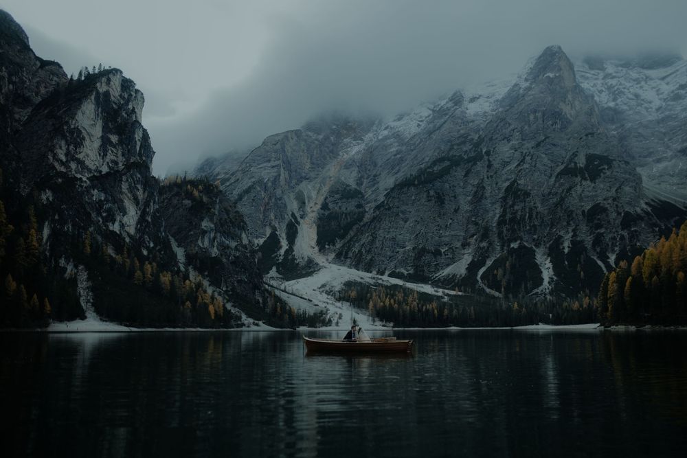 Dramatic mountain lake landscape with snow-capped peaks reflecting in calm waters at dusk.