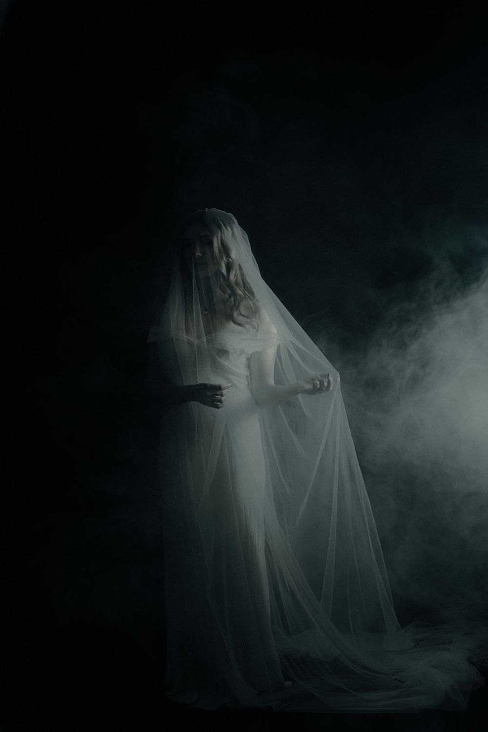 Ethereal bride in white shrouds emerge from dark misty background captured by a destination elopement photographer.