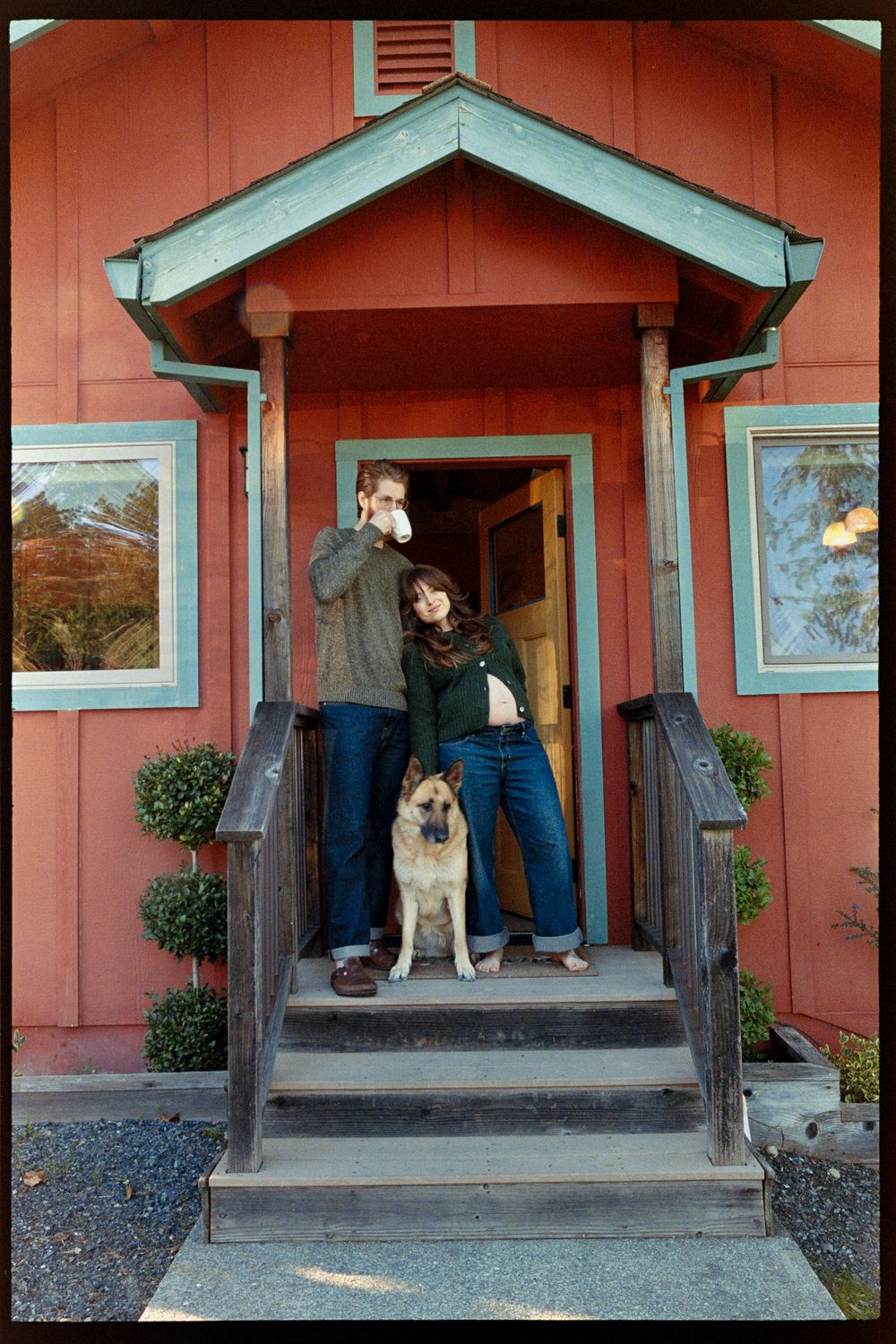 Couple with German Shepherd dog standing on porch steps of red craftsman house.
