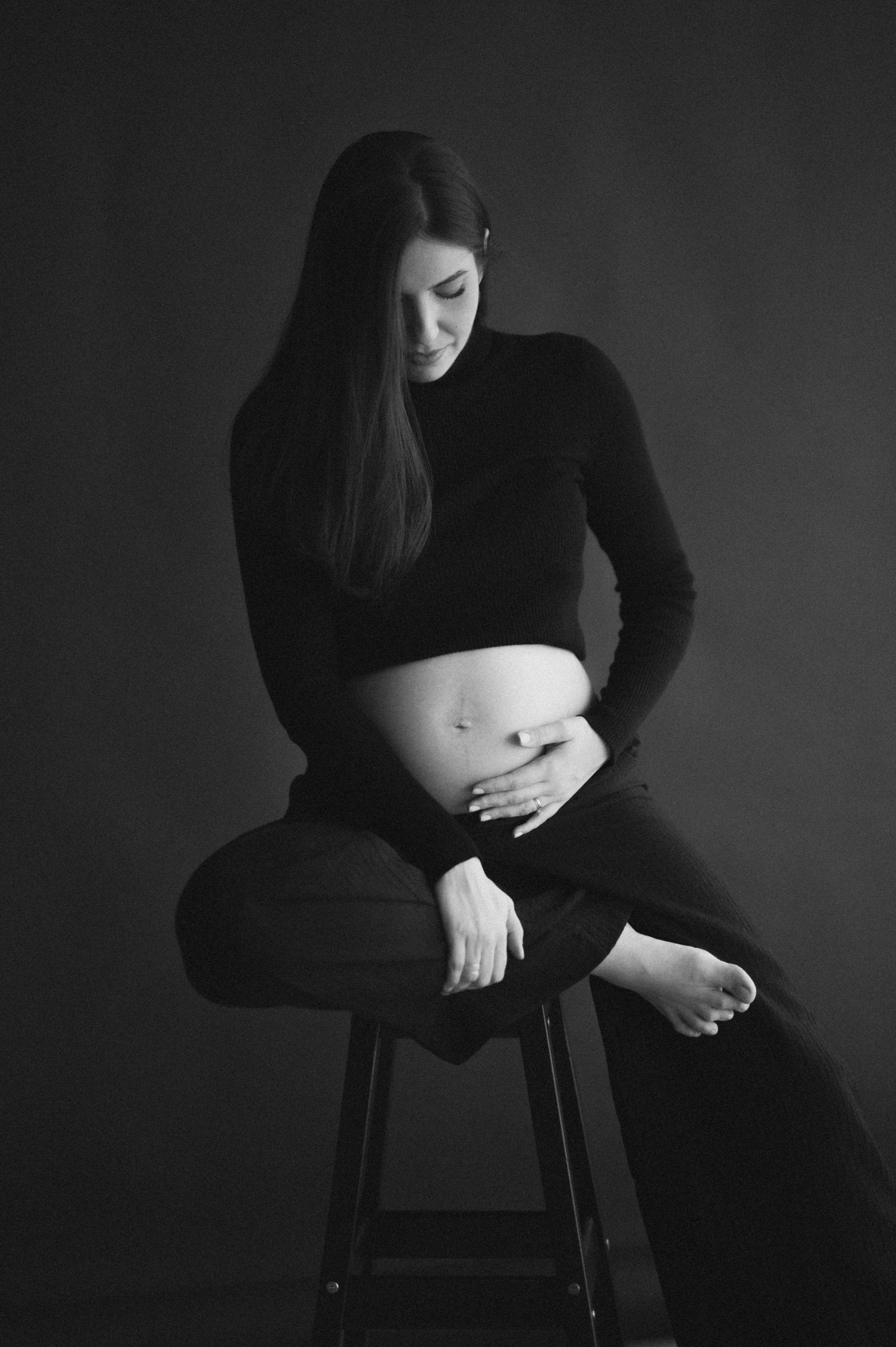 Black and white artistic portrait series showing a woman in dark clothing sitting on a stool against a dark background.