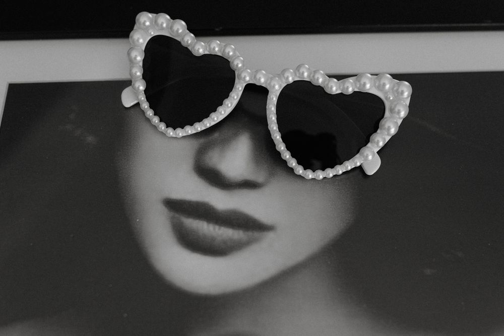 Heart-shaped pearl sunglasses resting on a black and white portrait photo of a glamorous woman.