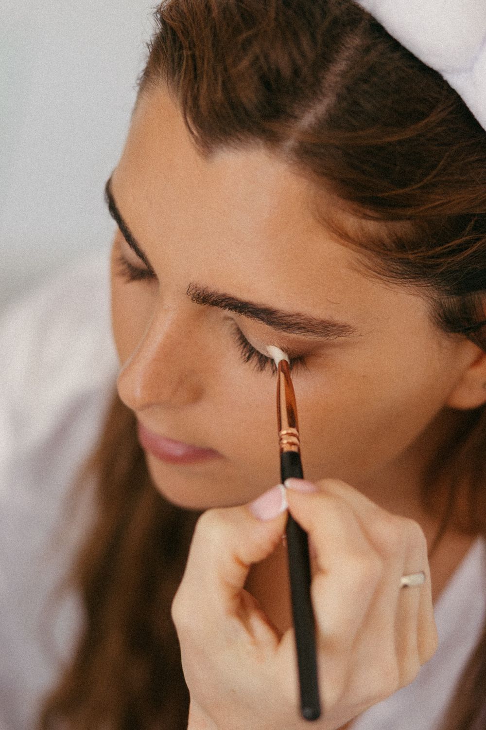 Woman applying eyeshadow with a makeup brush near her eye, wearing a white headband.