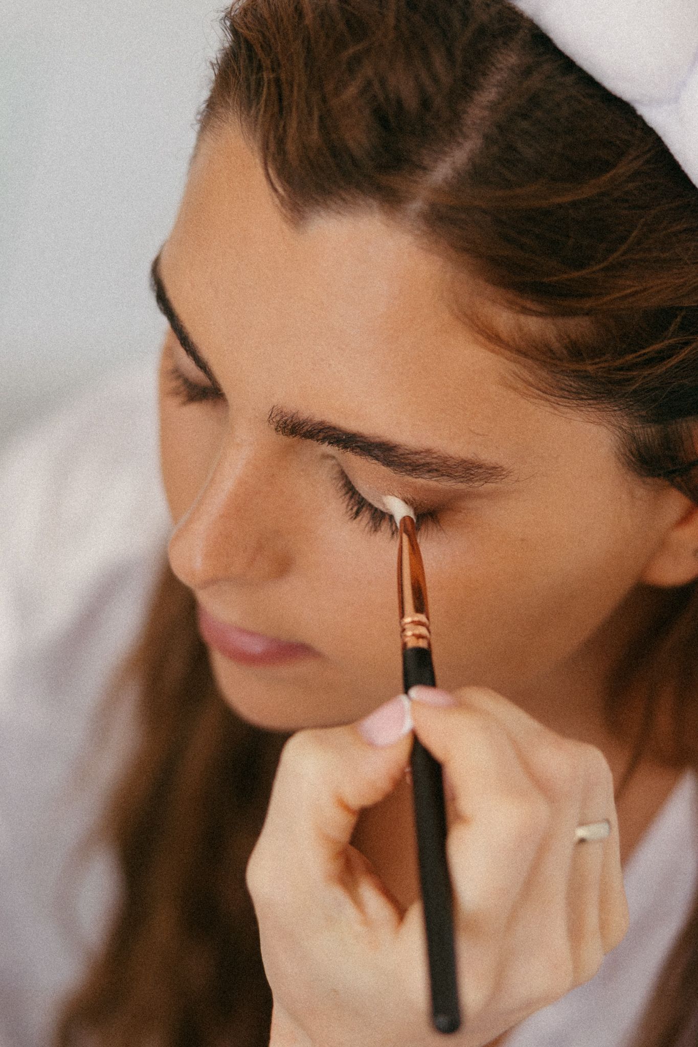 Woman applying eyeshadow with a makeup brush near her eye, wearing a white headband.