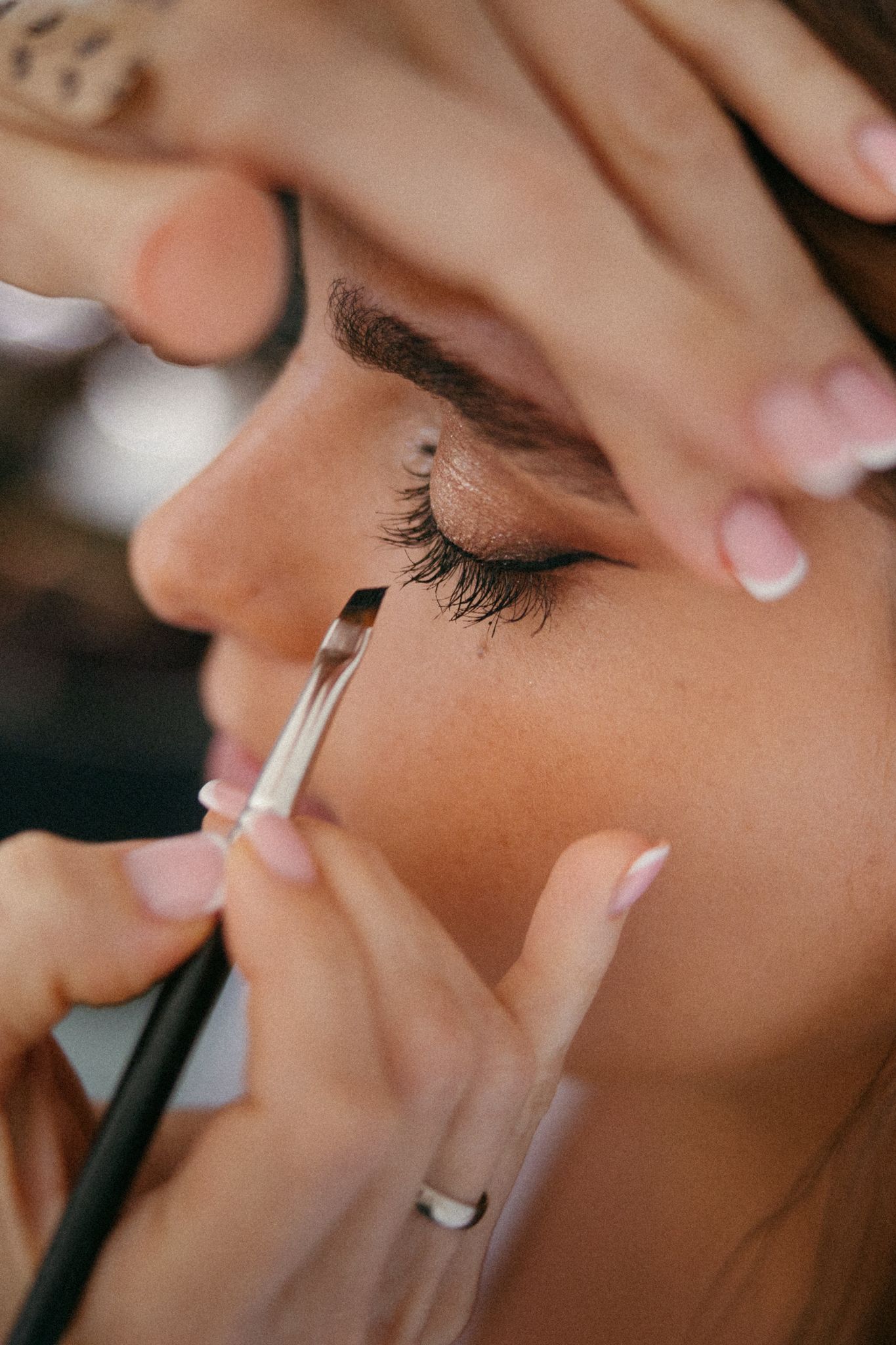 Close-up of a makeup artist applying eyeliner with a brush on a woman with long lashes and defined brows.