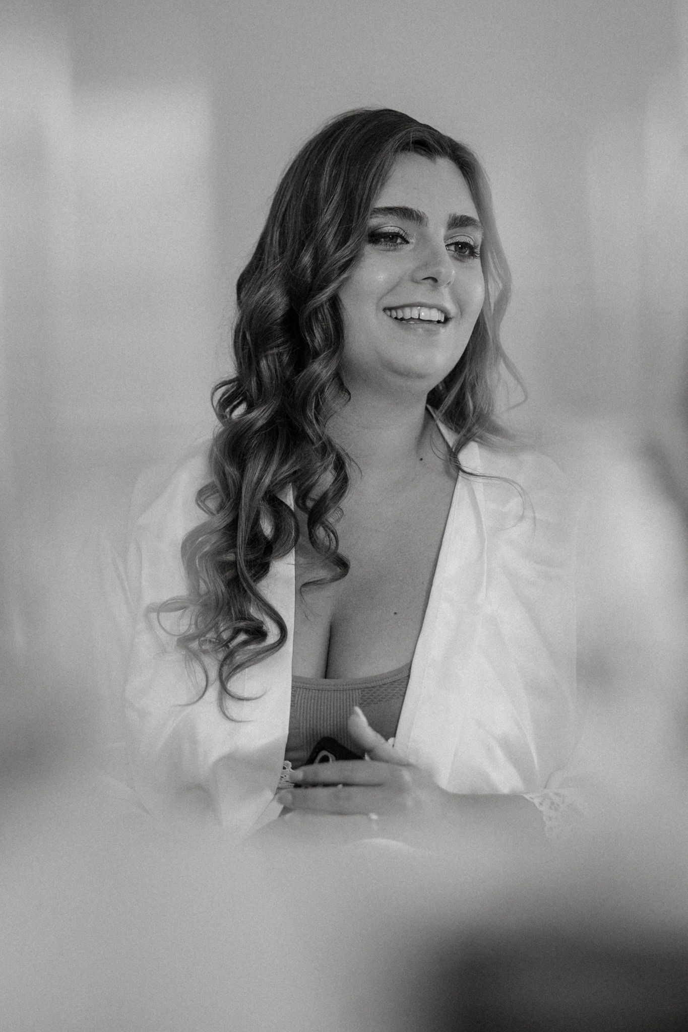 Black and white photo of a smiling woman with curly hair wearing a white robe, captured in a candid moment.