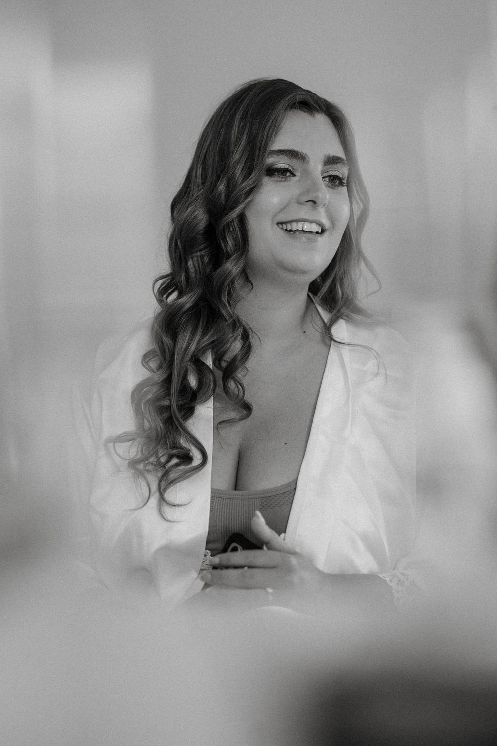 Black and white photo of a smiling woman with curly hair wearing a white robe, captured in a candid moment.