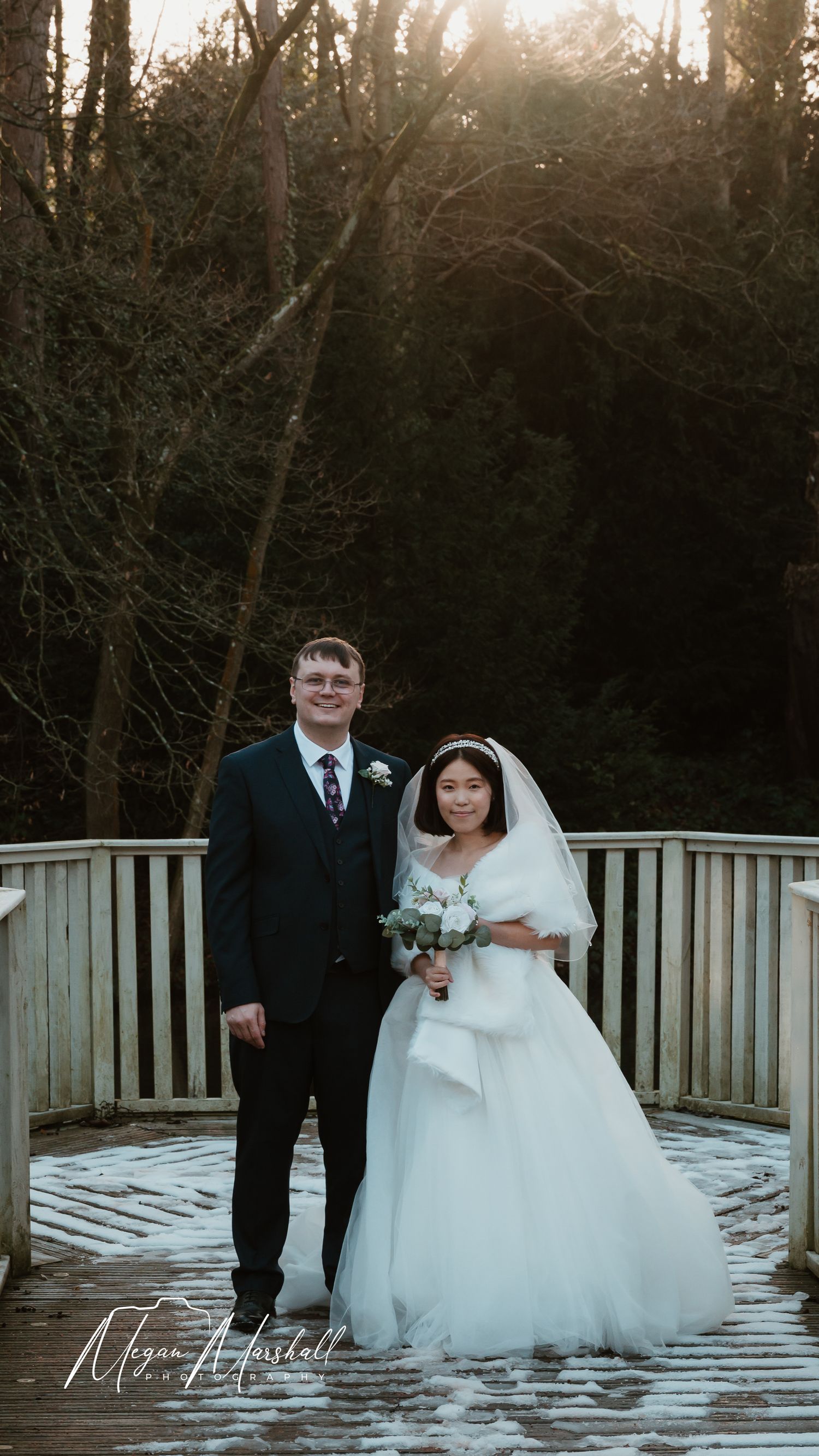 Bride and groom standing in snow-covered garden outside elegant stone manor house wedding venue in winter.