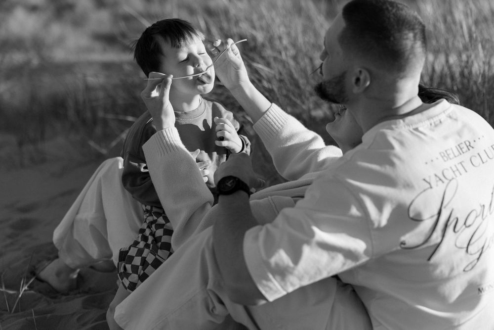 Black and white photo of a man and child sitting outdoors, sharing a playful moment together.