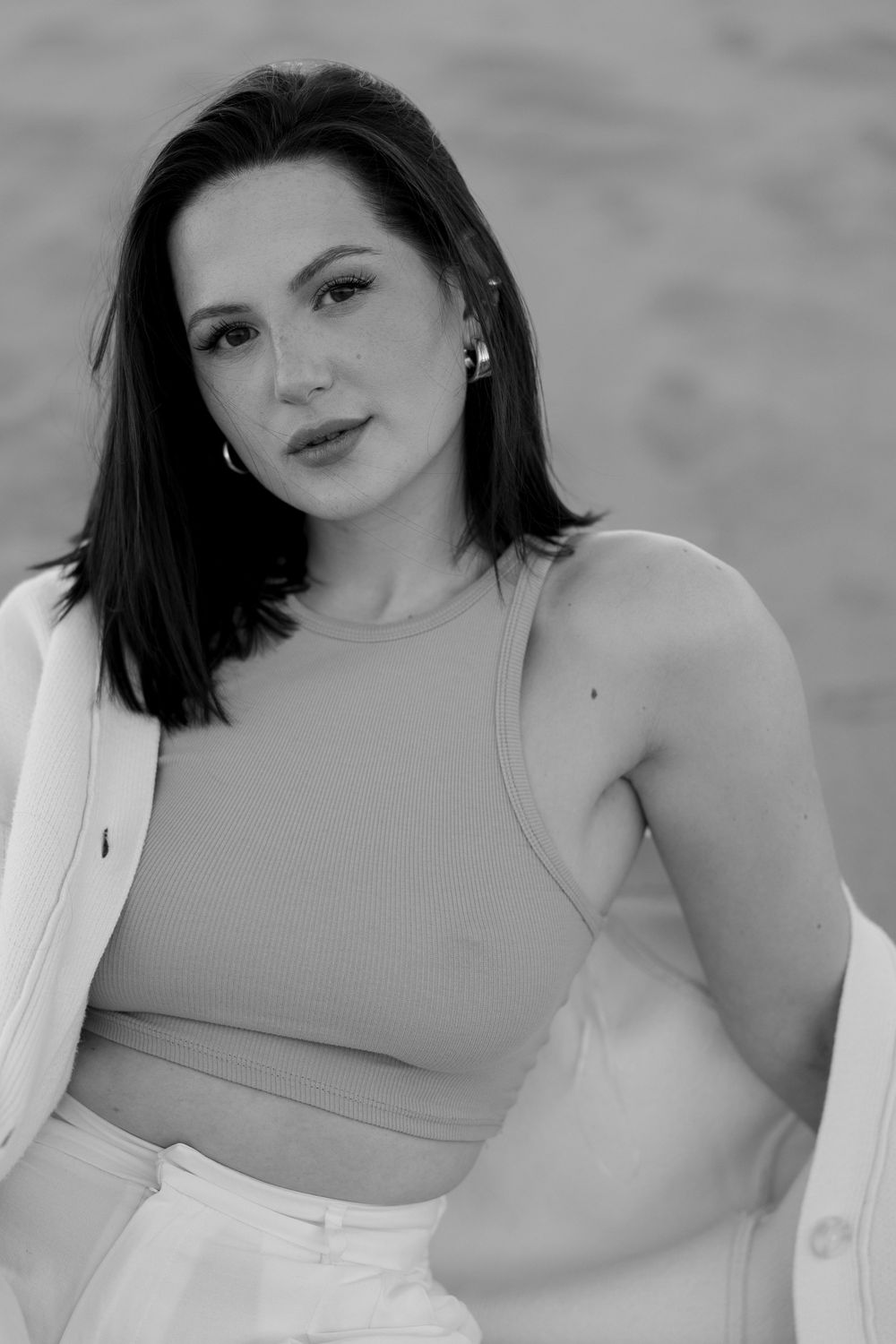 Black and white portrait of a young woman with dark hair wearing a crop top and white jacket outdoors.