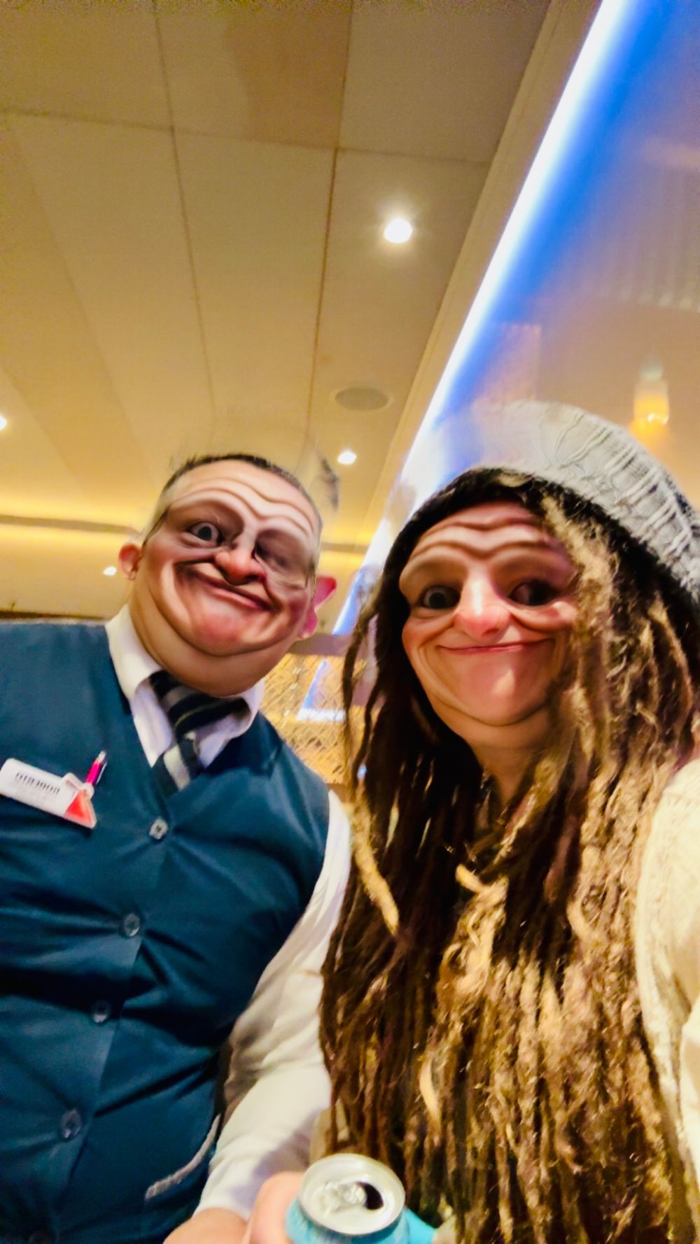Two people posing with funny face filter selfie inside cruise ship bar, one wearing staff uniform.