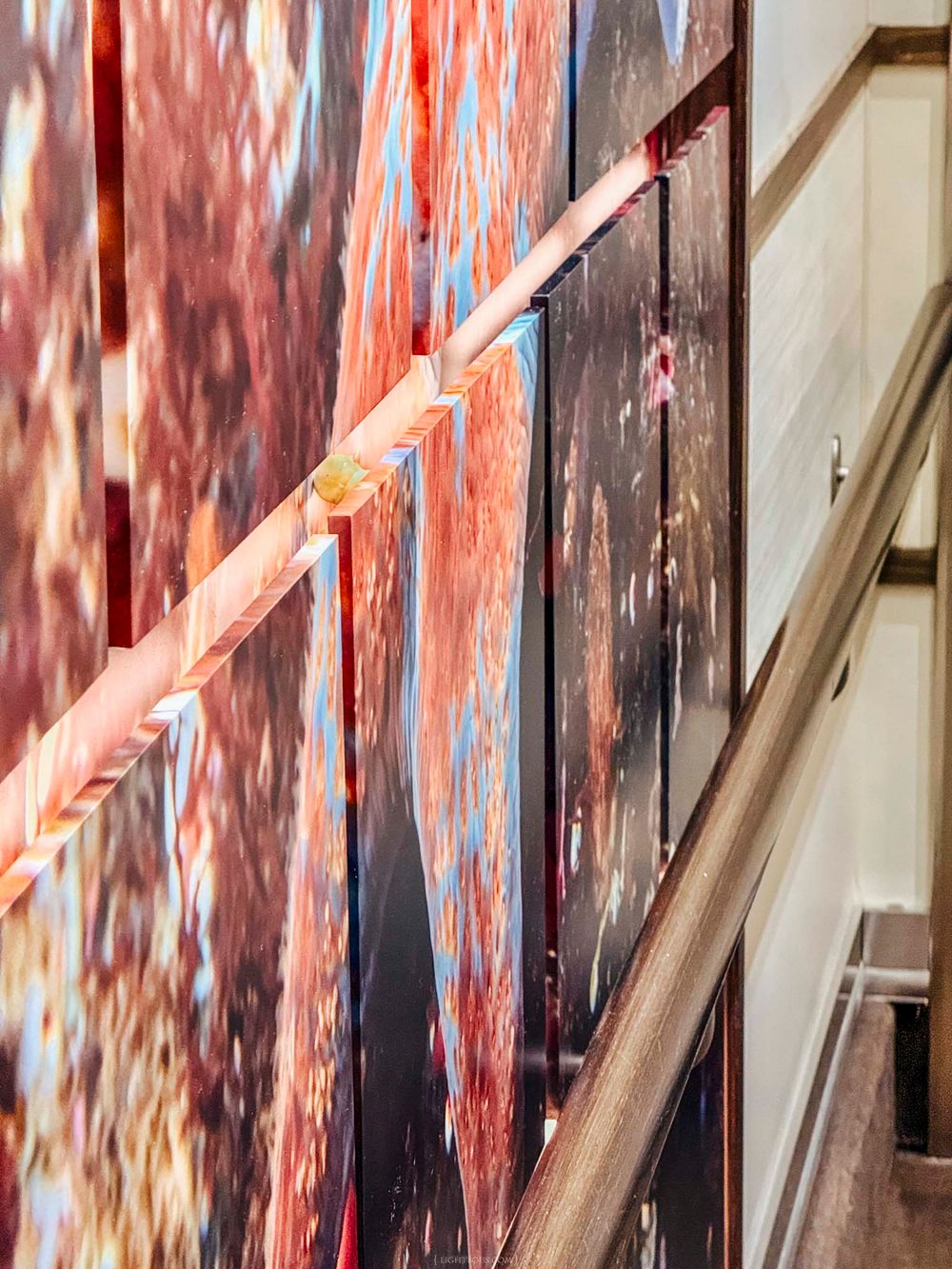 Abstract red and blue large-scale artwork panels displayed along a staircase wall with metal handrail.