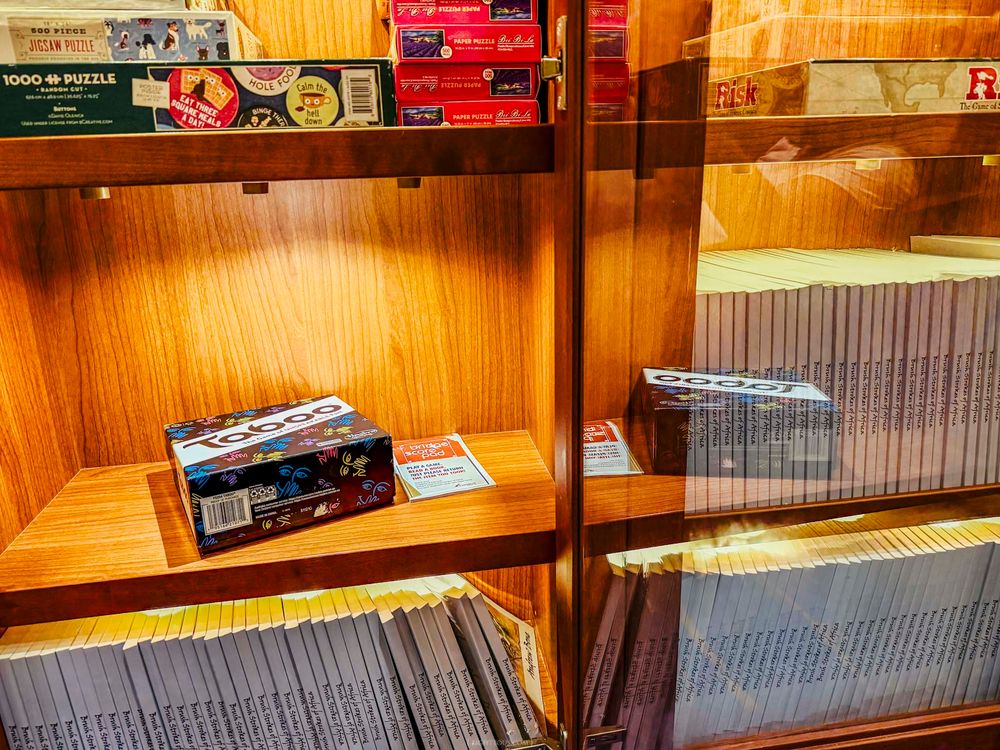 Wooden display cabinet with glass shelves holding board games, puzzles, and stacked media cases in an organized retail setting.