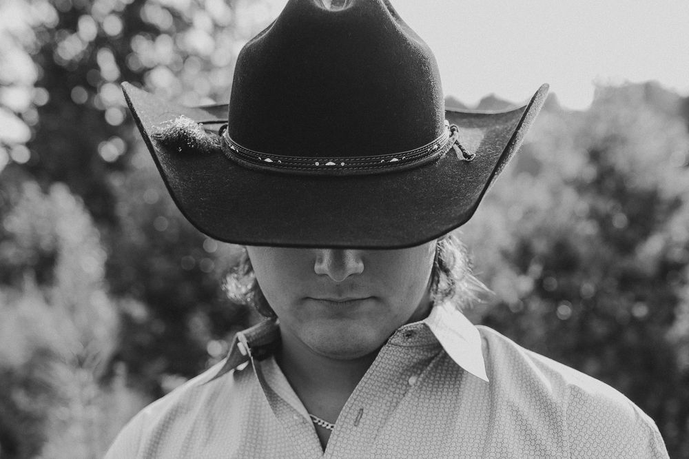 A black and white photo of equestrians in cowboy hats and riding gear walking in line on a sunny day.