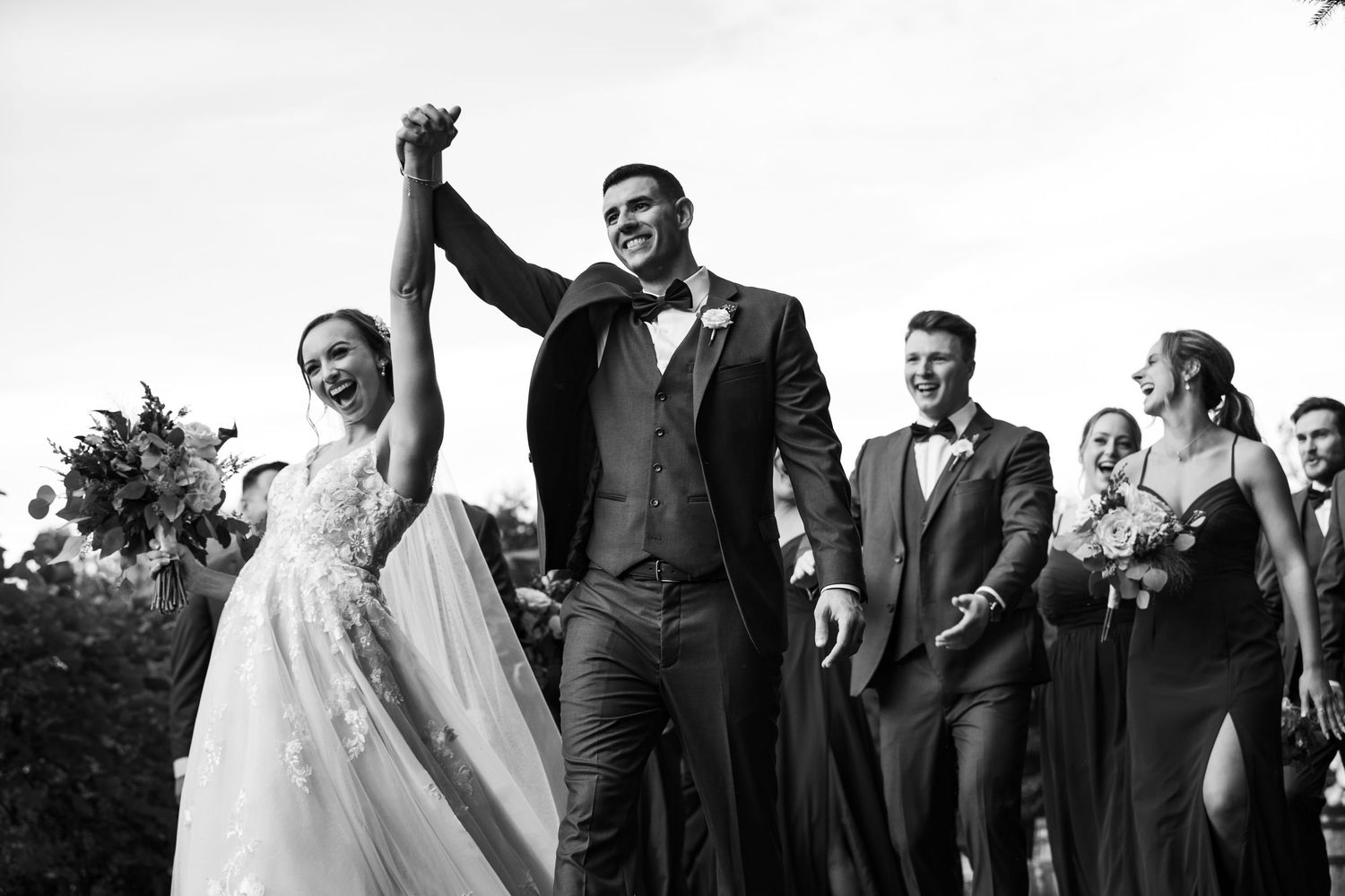Black and white photo of bride, groom, and bridal party cheering at Birchwood Vineyard in Derry, NH.