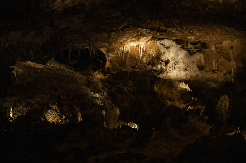 Illuminated stalactites and rock formations inside a dark cave, highlighting natural mineral deposits.