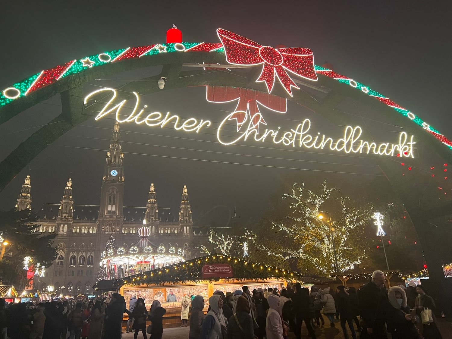 Illuminated Wiener Christkindlmarkt Christmas market sign at night with Vienna City Hall lit up in background.