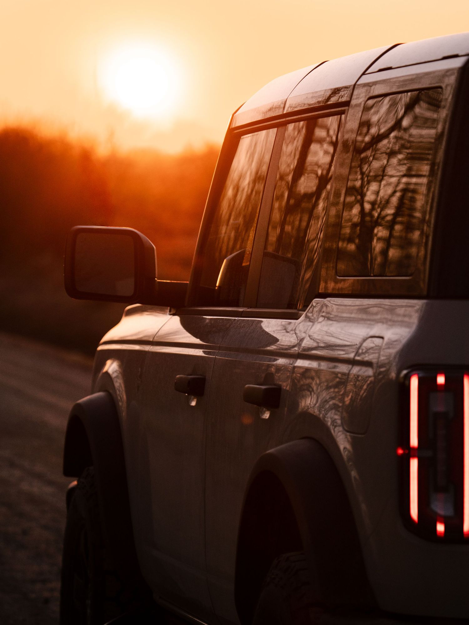 A rugged SUV silhouetted against a golden sunset on a scenic road, with warm orange hues illuminating the sky.