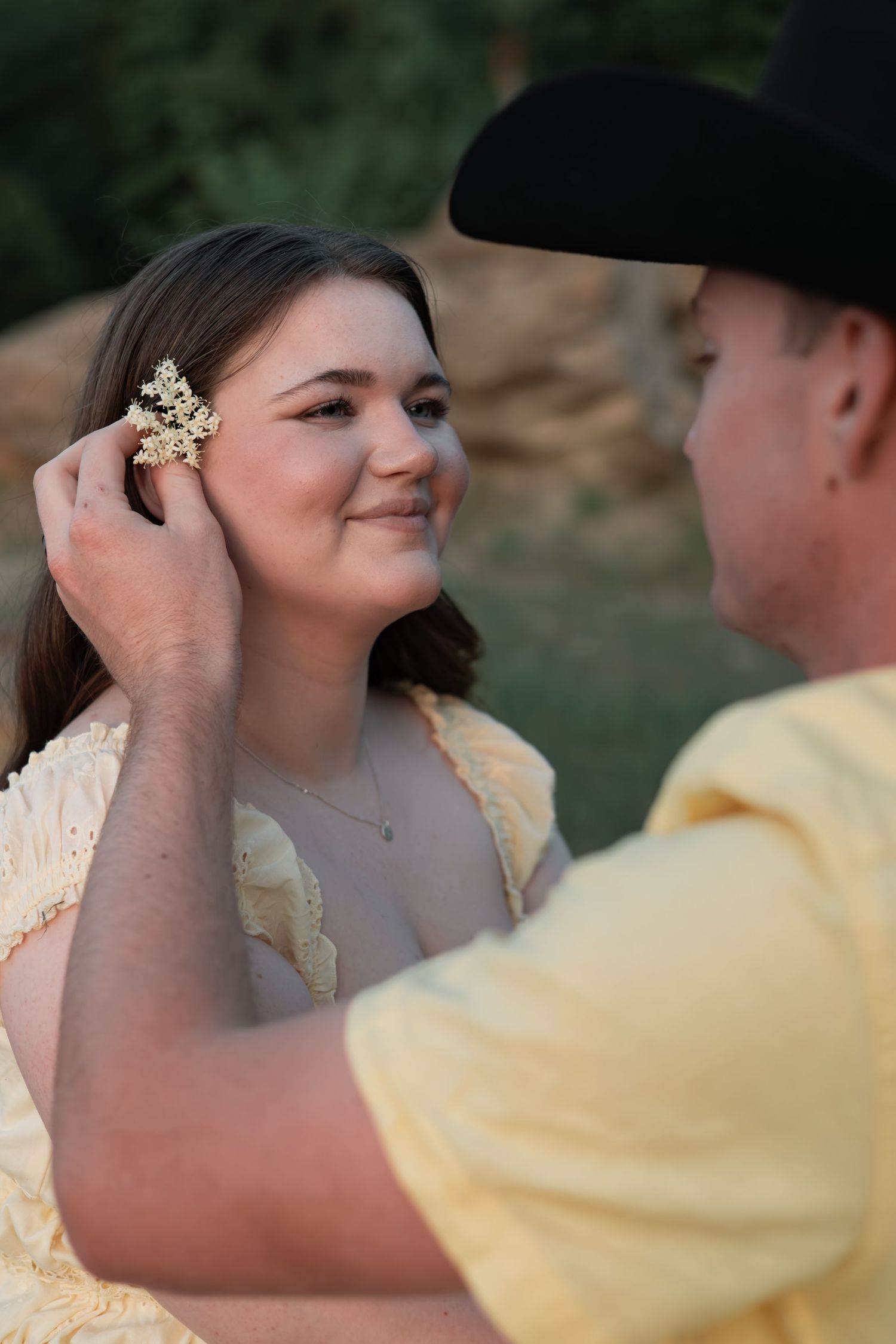 Couple sharing a romantic kiss at golden hour in a sunlit green field, woman in white dress with one leg lifted.