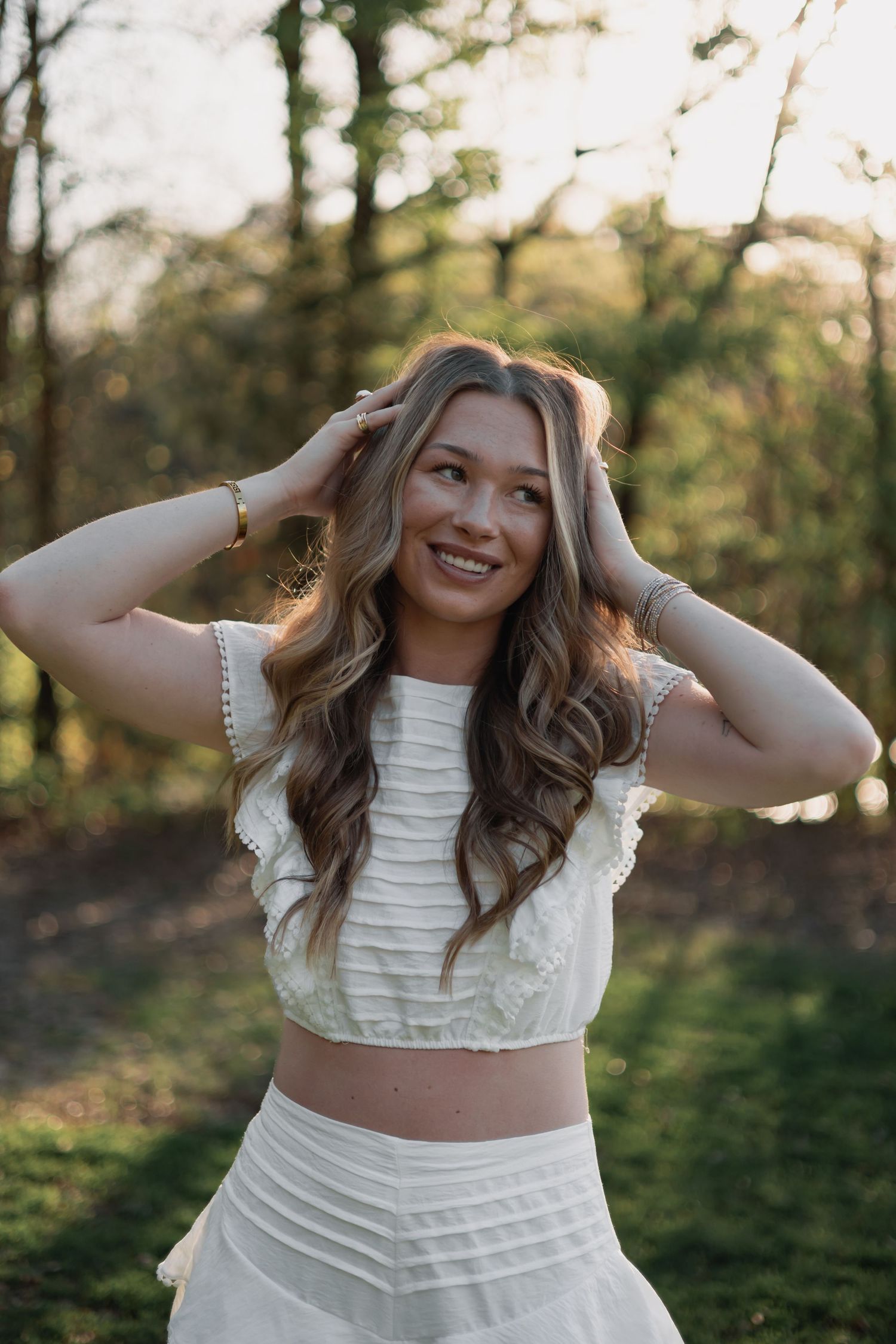 Woman in polka dot top and jeans leaning back on rocks at sunset with trees in background.