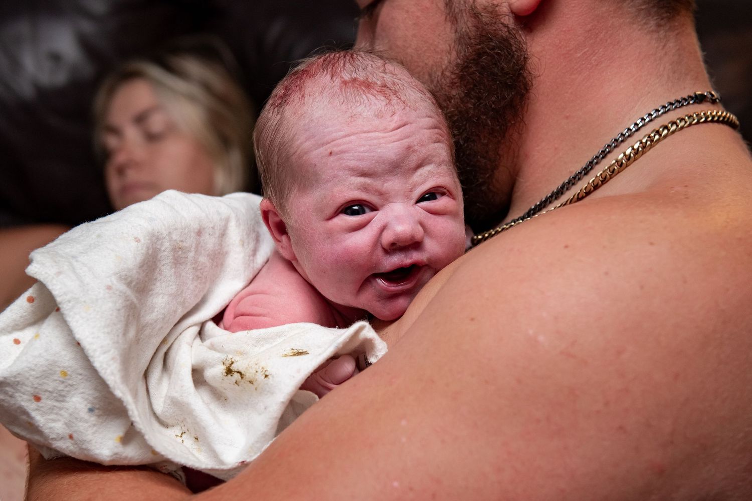 A newborn baby is shown in multiple photos crying and making different facial expressions while wrapped in white blankets.