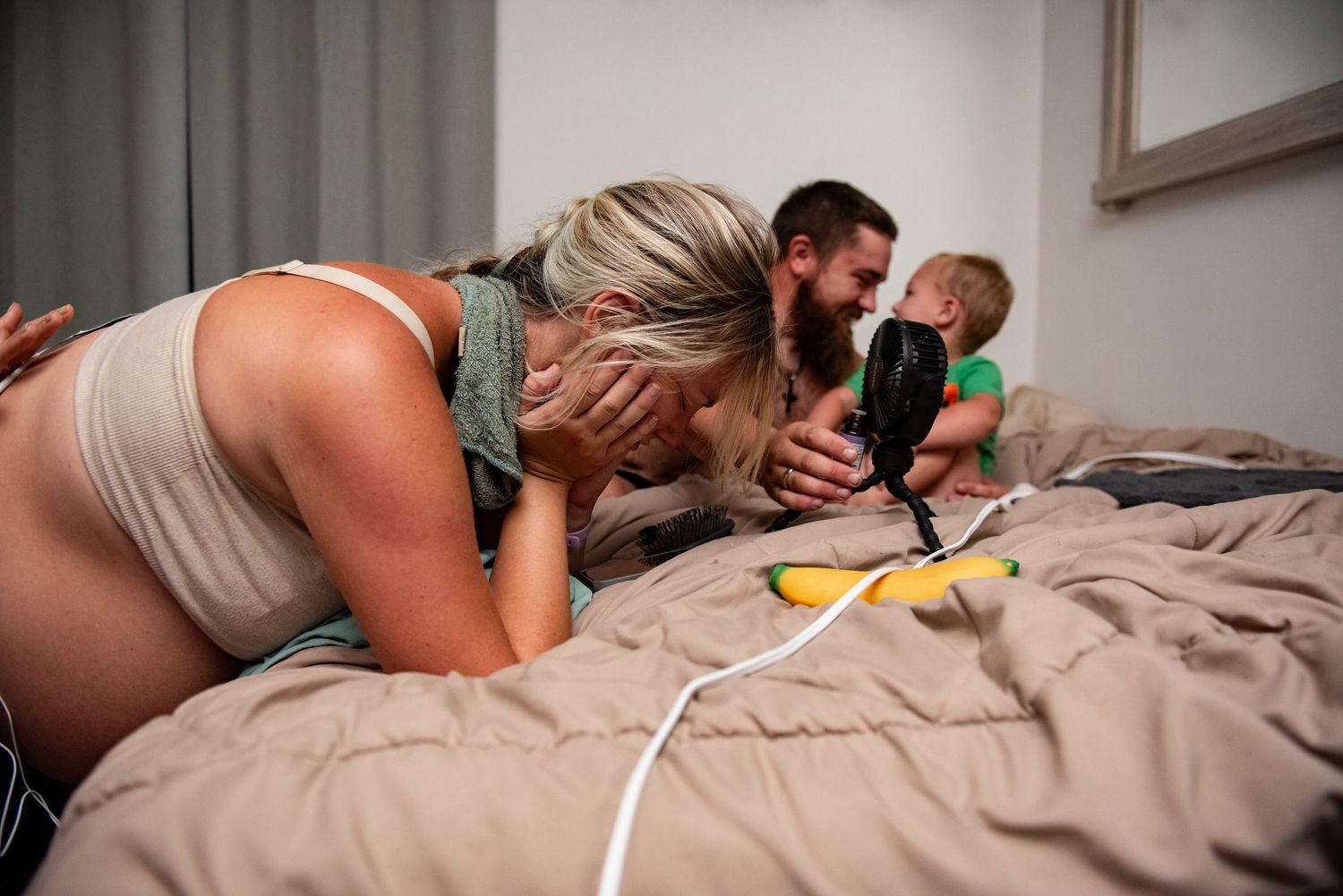 A pregnant person experiencing labor contractions leans on a birthing ball while receiving support at home.