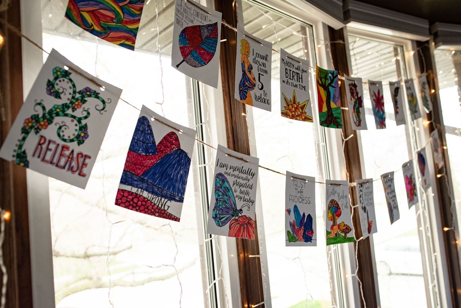 Colorful affirmation cards for labor hanging on strings across a sunny window.