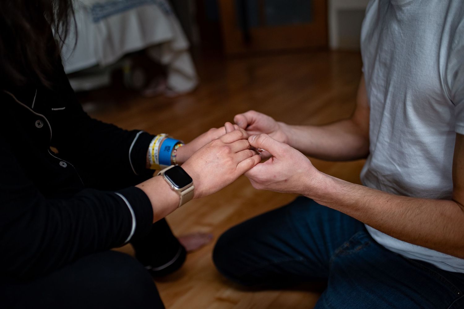 Close-up view of hands holding a smartphone and scrolling on a wooden surface in low light conditions.