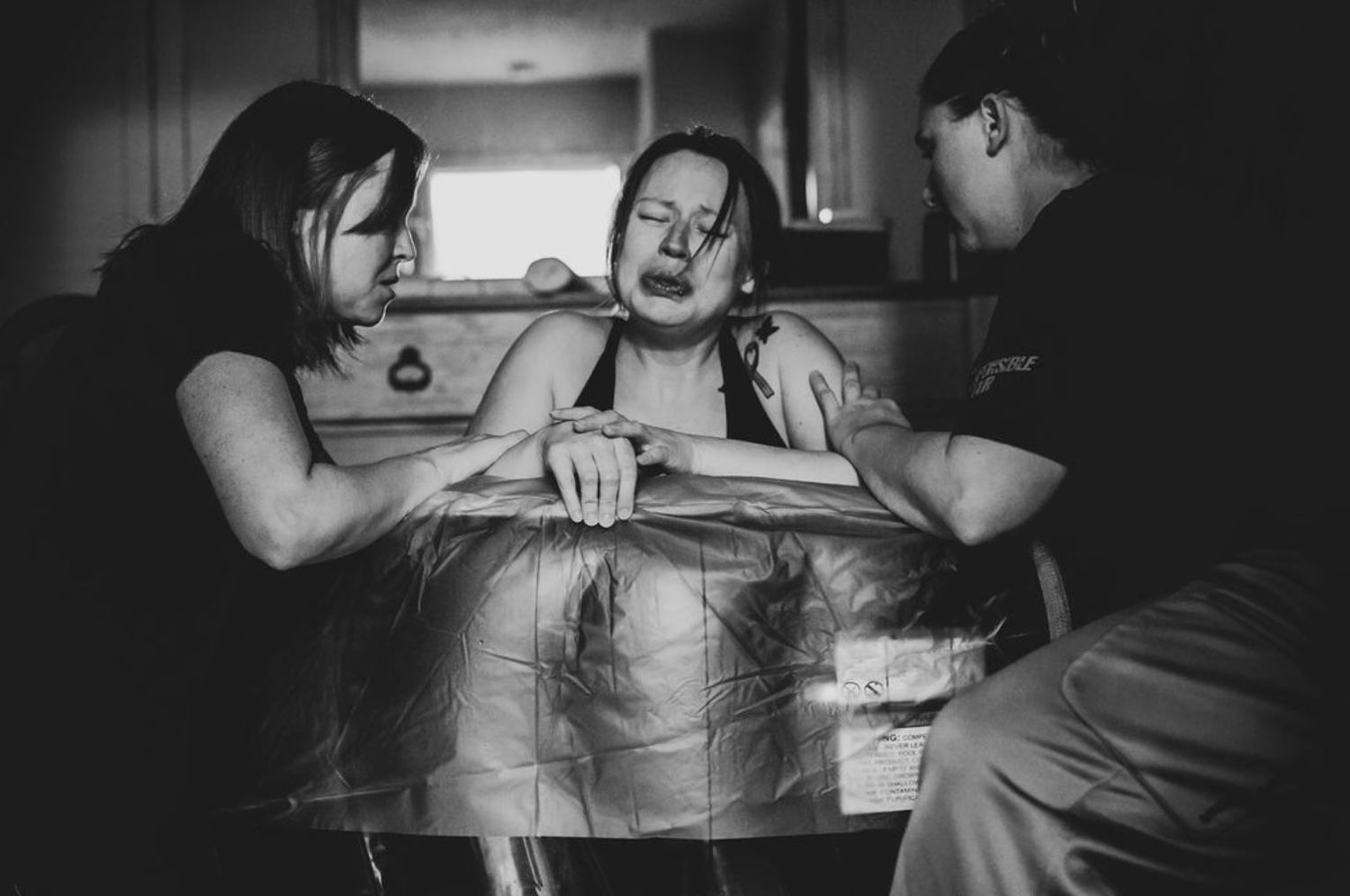 A dramatic black and white capture of labor support during childbirth.