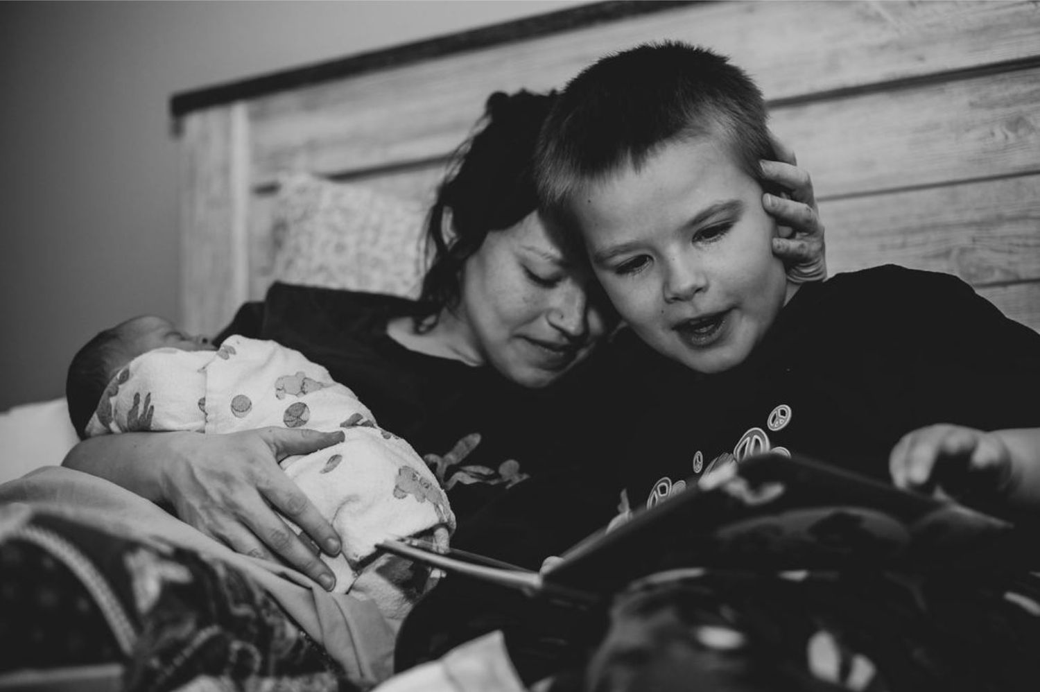 Black and white intimate family moment with newborn baby looking at device.