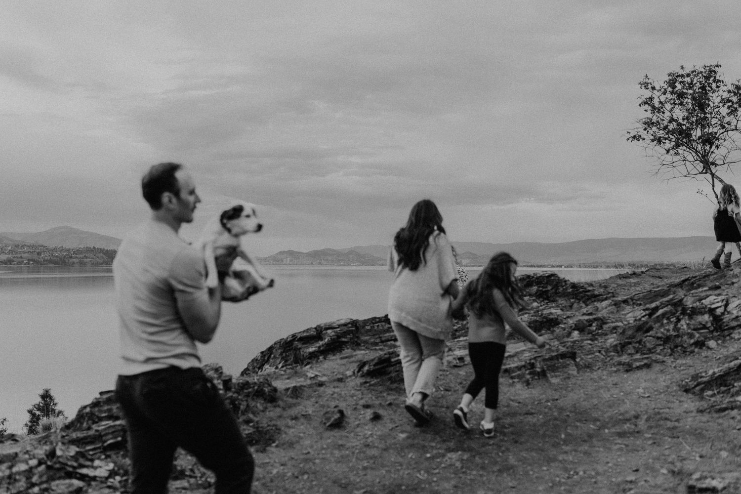 Black and white photo of a family with a dog hiking on a rocky trail overlooking a scenic lake.