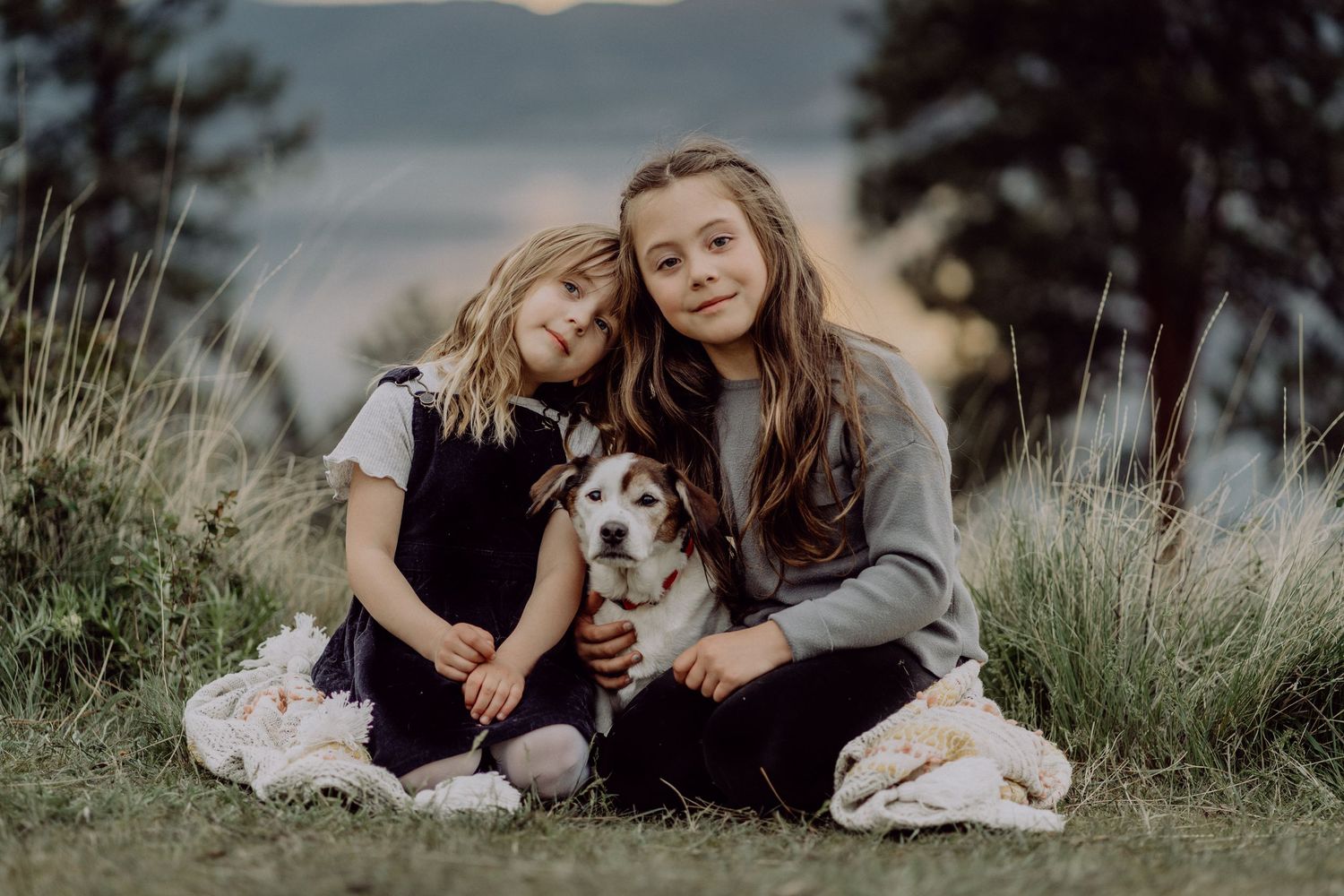 Two girls sitting on grass outdoors with a beagle dog, posing for a portrait photo in a natural setting.
