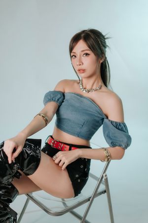 Vivienna Lai 個人品牌形象照Young woman in blue off-shoulder crop top, black mini skirt, and red belt sits on a chair in a studio.