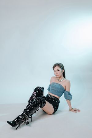 專業人像攝影，展現藝人獨特氣質Young woman in blue off-shoulder top, black shorts, and thigh-high patent boots posing on white studio floor.