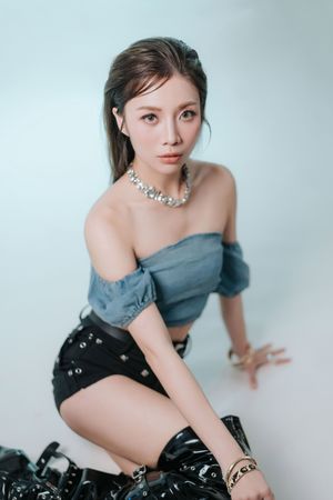 女團風格人像拍攝，呈現自信舞台感Young Asian woman in off-shoulder denim top, black mini skirt, boots, and pearl necklace poses on white studio floor.