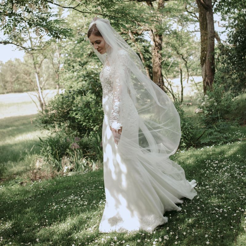 Black and white photo of a bride in lace dress and veil, surrounded by dreamy floral double exposure effect outdoors.