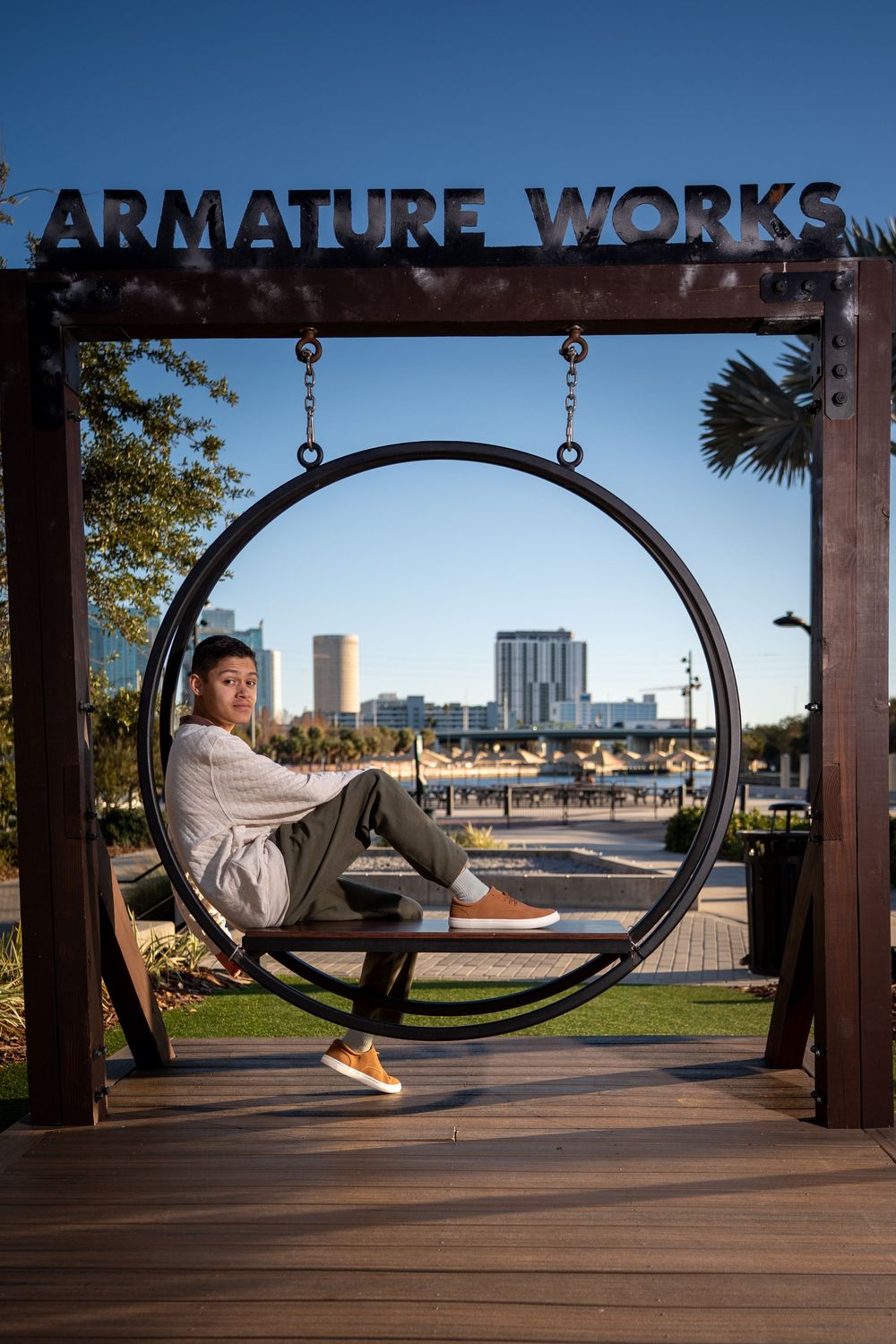 Person sitting in a circular swing at Armature Works Tampa with city skyline in background.