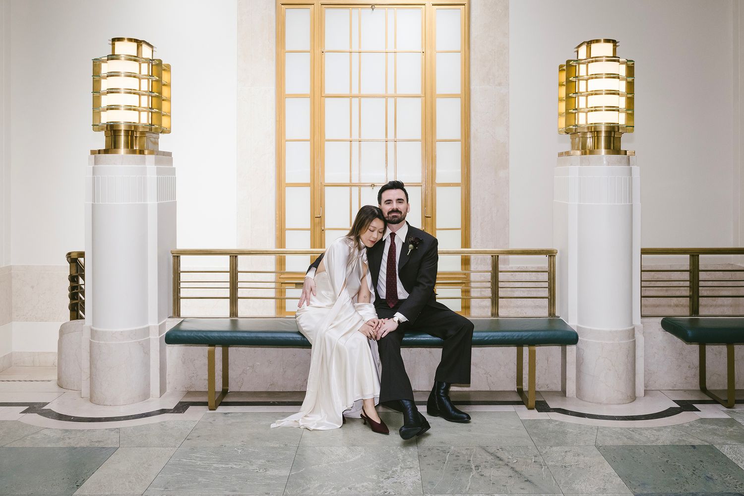 Elegant bride and groom walking hand in hand through a grand marble hallway after their wedding ceremony.