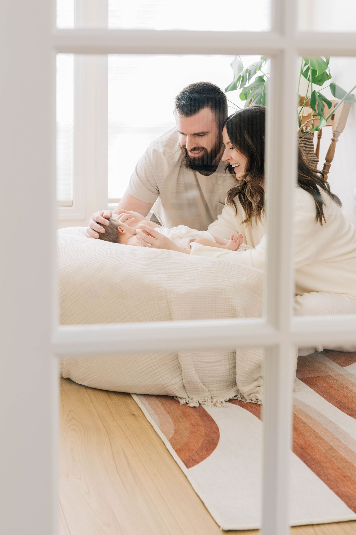 Happy parents lying on floor smiling at their newborn baby in a bright, cozy bedroom.
