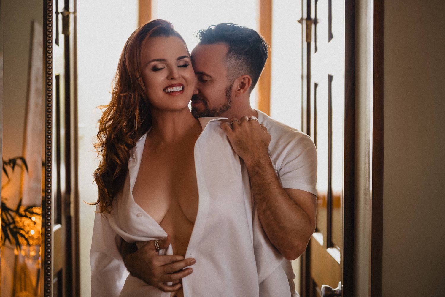 Romantic couple embracing and smiling in warm sunlight, woman in white shirt, man kissing her cheek. intimate couples photoshoot new orleans