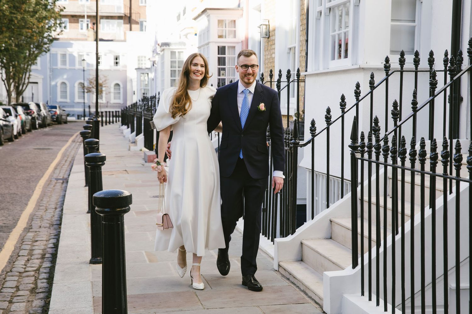 Bride and groom walking hand in hand along a London street on their wedding day.