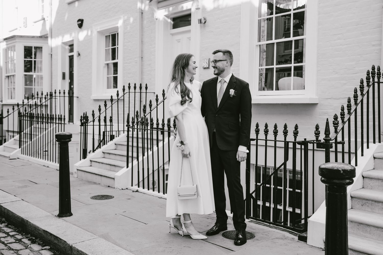 Elegant couple in wedding attire posing on a classic London street in black and white photo.