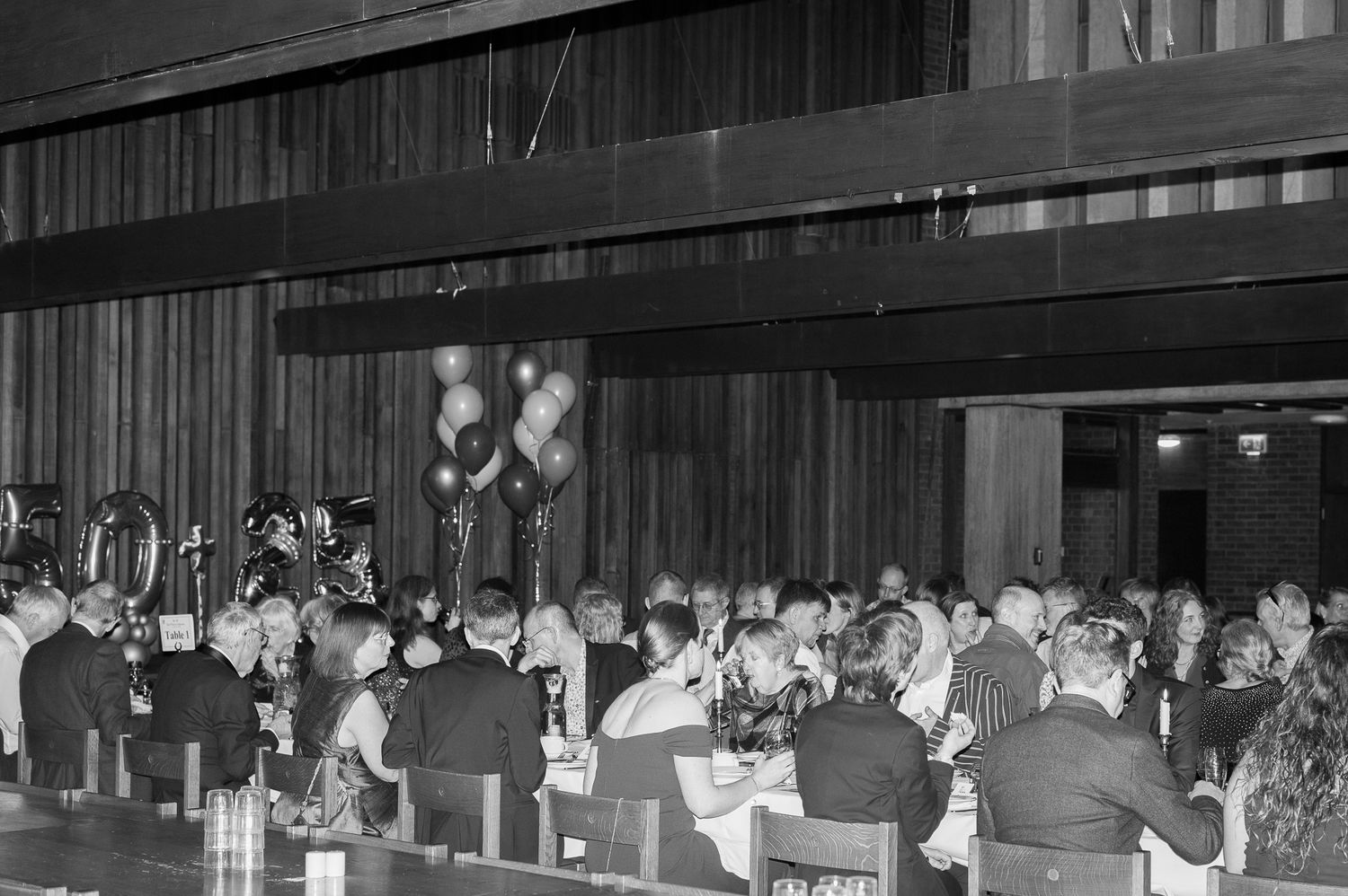 Black and white photo of a large formal banquet hall filled with guests seated at tables decorated with balloons.