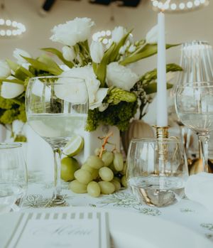 Elegant wedding table setting with white roses, green grapes, crystal glasses, and a tall white candle centerpiece.
