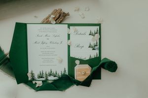 Elegant green wedding invitation suite with pine tree design, ring box, and ribbon on white background.