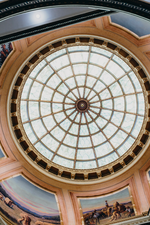 Ornate glass dome ceiling with golden trim and circular skylight in a grand historic building.