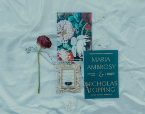 Elegant wedding invitation suite for Maria Ambrosy and Nicholas Topping with floral accents on white fabric.