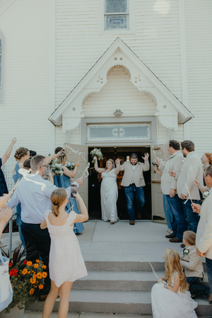 Joyful newlyweds exit a white chapel as guests celebrate their wedding with streamers and cheers.