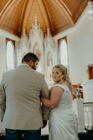 Bride and groom standing at church altar, bride smiling back at camera in white gown.